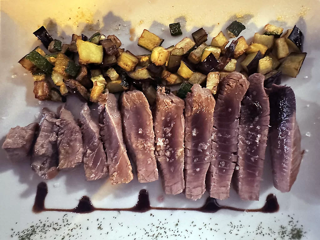 seared tuna steak sliced on a plate with grilled vegetables