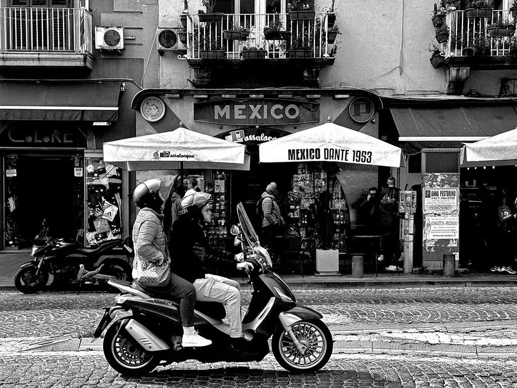 black and white image of people on a motorcycle in front of cafe mexico naples