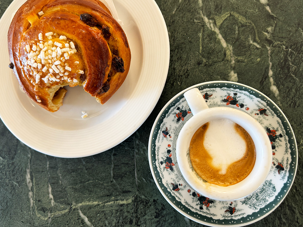 espresso macchiato in a cup and a pastry with a bite taken out